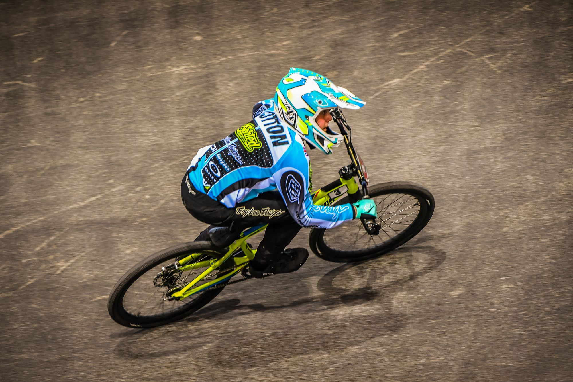 Charlie Cotton leaning his lime-green BMX race bike hard through a berm in his aqua Sorted Racegear kit