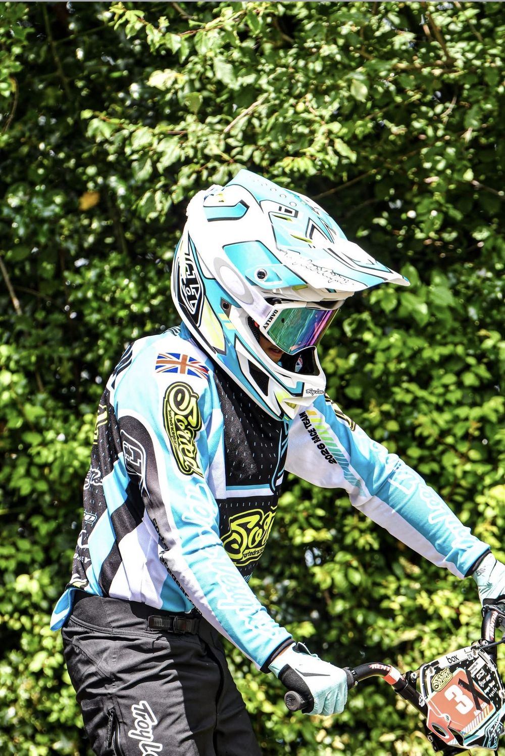 Charlie in his aqua and white full-face helmet and goggles, gripping the bars